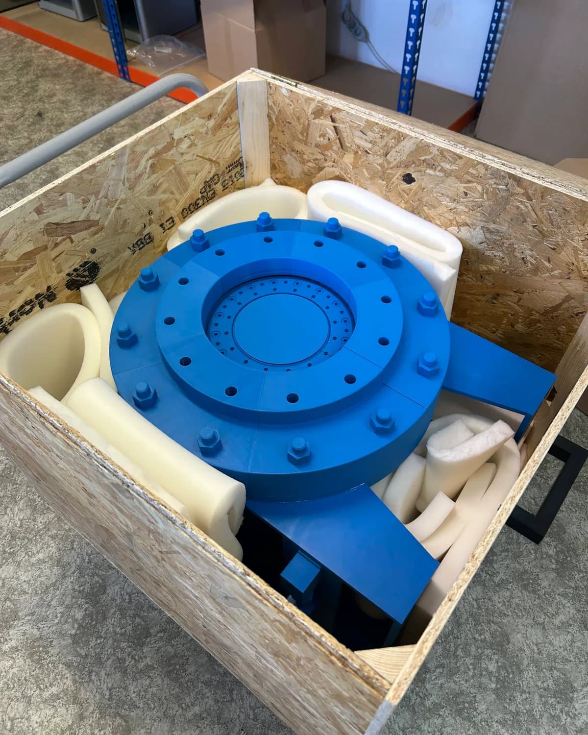 Model uzávěru zafixovaný v dřevěné bedně z OSB desek, obložený pěnovými výplněmi, s madly po stranách.