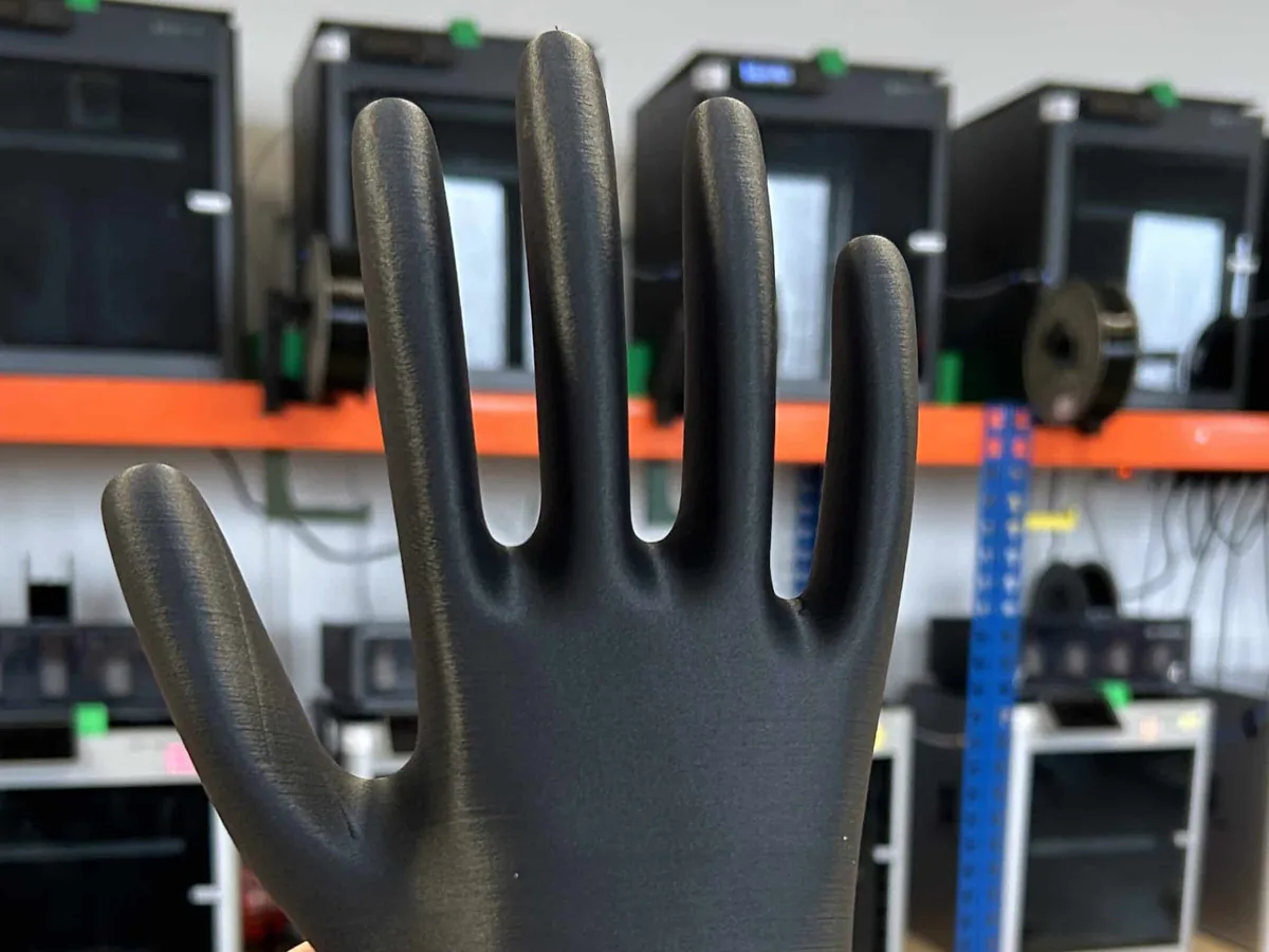 Černá tištěná forma ve tvaru ruky držená proti regálu s tiskárnami.